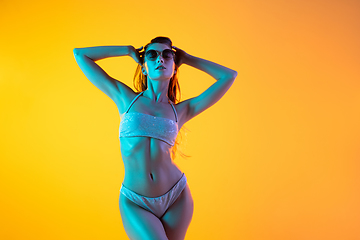 Image showing Fashion portrait of seductive girl in stylish swimwear posing on a bright yellow background. Summertime, beach season