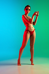 Image showing Fashion portrait of seductive girl in stylish swimwear posing on a bright gradient background. Summertime, beach season