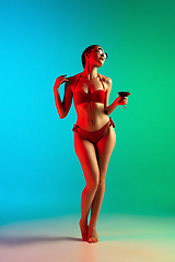 Image showing Fashion portrait of seductive girl in stylish swimwear posing on a bright gradient background. Summertime, beach season