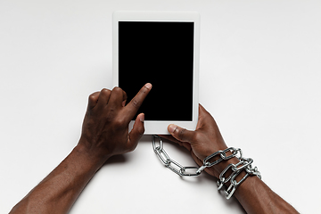 Image showing Close up of human hand using tablet with blank black screen. Tied with chain, addiction