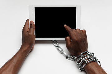 Image showing Close up of human hand using tablet with blank black screen. Tied with chain, addiction