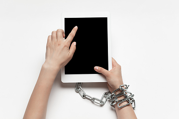 Image showing Close up of human hand using tablet with blank black screen. Tied with chain, addiction