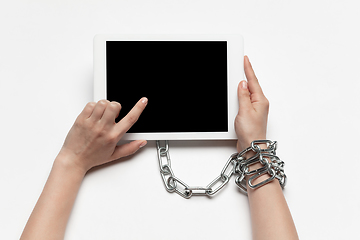 Image showing Close up of human hand using tablet with blank black screen. Tied with chain, addiction