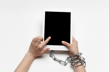 Image showing Close up of human hand using tablet with blank black screen. Tied with chain, addiction