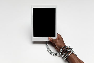 Image showing Close up of human hand using tablet with blank black screen. Tied with chain, addiction