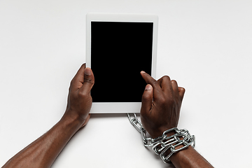 Image showing Close up of human hand using tablet with blank black screen. Tied with chain, addiction