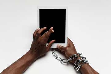 Image showing Close up of human hand using tablet with blank black screen. Tied with chain, addiction