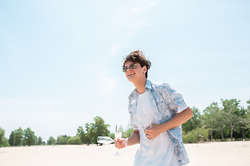 Image showing Seasonal feast at beach resort. Happy stylish boy celebrating, resting, having fun on the beach in sunny summer day