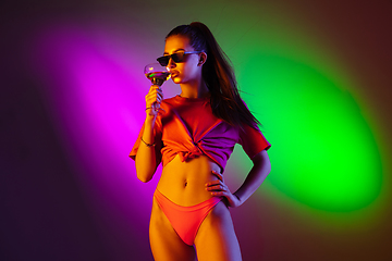 Image showing Beautiful seductive girl in fashionable swimsuit on disco bicolored neon studio background in neon light. Summer, resort, fashion and weekend concept