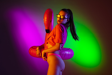 Image showing Beautiful seductive girl in fashionable swimsuit on disco bicolored neon studio background in neon light. Summer, resort, fashion and weekend concept