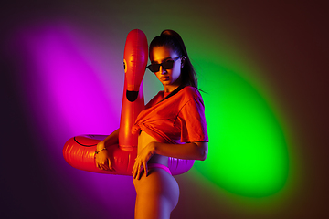 Image showing Beautiful seductive girl in fashionable swimsuit on disco bicolored neon studio background in neon light. Summer, resort, fashion and weekend concept