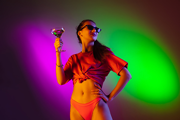 Image showing Beautiful seductive girl in fashionable swimsuit on disco bicolored neon studio background in neon light. Summer, resort, fashion and weekend concept