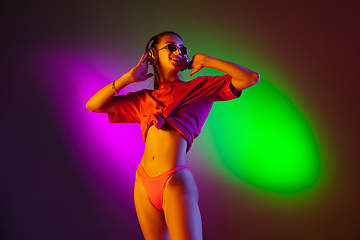 Image showing Beautiful seductive girl in fashionable swimsuit on disco bicolored neon studio background in neon light. Summer, resort, fashion and weekend concept