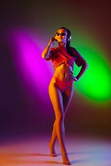 Image showing Beautiful seductive girl in fashionable swimsuit on disco bicolored neon studio background in neon light. Summer, resort, fashion and weekend concept