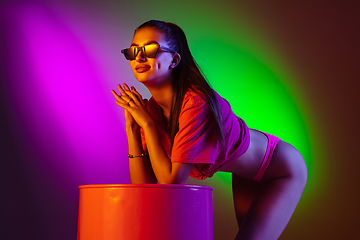 Image showing Beautiful seductive girl in fashionable swimsuit on disco bicolored neon studio background in neon light. Summer, resort, fashion and weekend concept