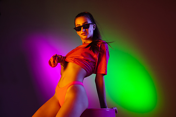 Image showing Beautiful seductive girl in fashionable swimsuit on disco bicolored neon studio background in neon light. Summer, resort, fashion and weekend concept