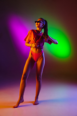 Image showing Beautiful seductive girl in fashionable swimsuit on disco bicolored neon studio background in neon light. Summer, resort, fashion and weekend concept