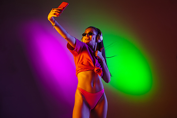 Image showing Beautiful seductive girl in fashionable swimsuit on disco bicolored neon studio background in neon light. Summer, resort, fashion and weekend concept