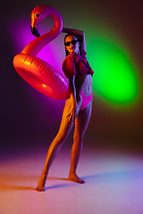 Image showing Beautiful seductive girl in fashionable swimsuit on disco bicolored neon studio background in neon light. Summer, resort, fashion and weekend concept