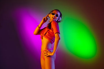 Image showing Beautiful seductive girl in fashionable swimsuit on disco bicolored neon studio background in neon light. Summer, resort, fashion and weekend concept