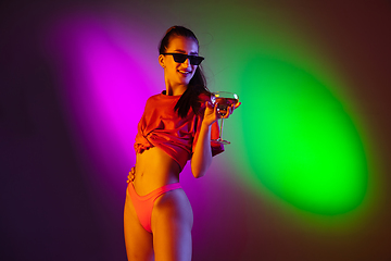 Image showing Beautiful seductive girl in fashionable swimsuit on disco bicolored neon studio background in neon light. Summer, resort, fashion and weekend concept