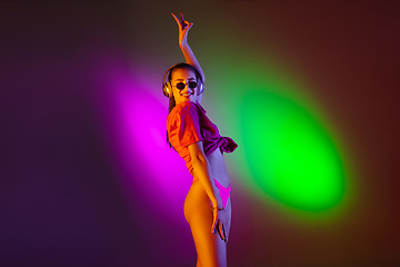 Image showing Beautiful seductive girl in fashionable swimsuit on disco bicolored neon studio background in neon light. Summer, resort, fashion and weekend concept