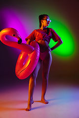 Image showing Beautiful seductive girl in fashionable swimsuit on disco bicolored neon studio background in neon light. Summer, resort, fashion and weekend concept