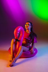 Image showing Beautiful seductive girl in fashionable swimsuit on disco bicolored neon studio background in neon light. Summer, resort, fashion and weekend concept