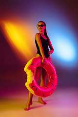 Image showing Beautiful seductive girl in fashionable swimsuit on disco bicolored neon studio background in neon light. Summer, resort, fashion and weekend concept