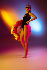 Image showing Beautiful seductive girl in fashionable swimsuit on disco bicolored neon studio background in neon light. Summer, resort, fashion and weekend concept