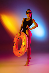 Image showing Beautiful seductive girl in fashionable swimsuit on disco bicolored neon studio background in neon light. Summer, resort, fashion and weekend concept