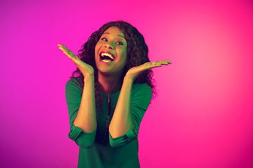 Image showing African-american young woman\'s portrait isolated on gradient pink background in neon light