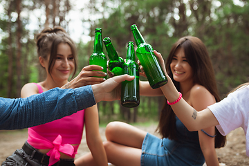 Image showing Group of friends clinking beer bottles during picnic in summer forest. Lifestyle, friendship