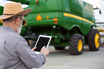 Image showing A farmer with a tractor, combine at a field in sunlight. Confident, bright colors