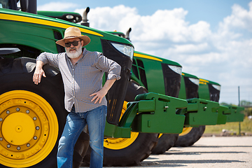 Image showing A farmer with a tractor, combine at a field in sunlight. Confident, bright colors