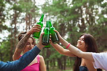 Image showing Group of friends clinking beer bottles during picnic in summer forest. Lifestyle, friendship