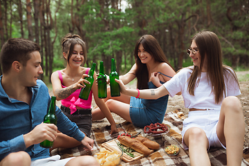 Image showing Group of friends clinking beer bottles during picnic in summer forest. Lifestyle, friendship