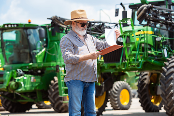 Image showing A farmer with a tractor, combine at a field in sunlight. Confident, bright colors