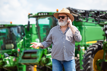 Image showing A farmer with a tractor, combine at a field in sunlight. Confident, bright colors