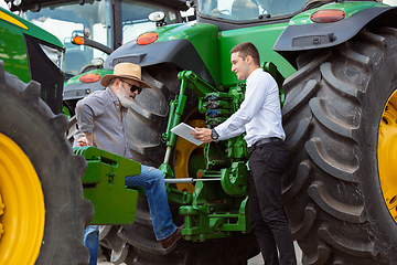 Image showing A farmer with a tractor, combine at a field in sunlight. Confident, bright colors