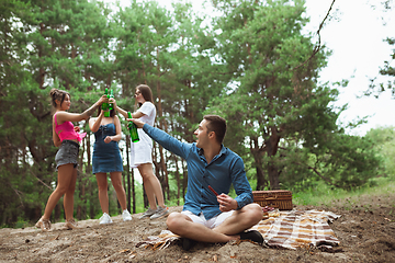 Image showing Group of friends clinking beer bottles during picnic in summer forest. Lifestyle, friendship