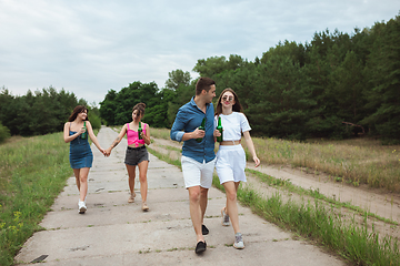 Image showing Group of friends clinking beer bottles during picnic in summer forest. Lifestyle, friendship