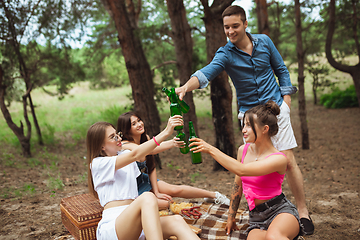 Image showing Group of friends clinking beer bottles during picnic in summer forest. Lifestyle, friendship