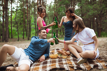 Image showing Group of friends clinking beer bottles during picnic in summer forest. Lifestyle, friendship