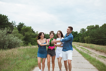 Image showing Group of friends clinking beer bottles during picnic in summer forest. Lifestyle, friendship