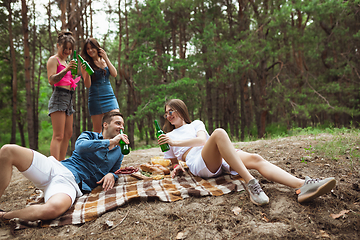 Image showing Group of friends clinking beer bottles during picnic in summer forest. Lifestyle, friendship