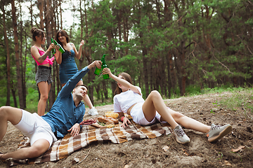 Image showing Group of friends clinking beer bottles during picnic in summer forest. Lifestyle, friendship