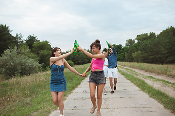 Image showing Group of friends clinking beer bottles during picnic in summer forest. Lifestyle, friendship