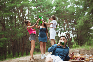 Image showing Group of friends clinking beer bottles during picnic in summer forest. Lifestyle, friendship