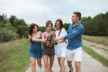 Image showing Group of friends clinking beer bottles during picnic in summer forest. Lifestyle, friendship